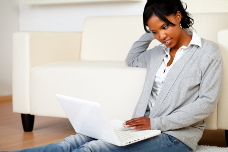 Portrait of a relaxed black woman browsing the Internet at home with her laptop while is sitting on the floor at home indoorの写真素材