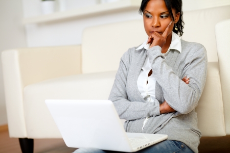 Portrait of a pensive young woman is sitting on the floor in front of her laptop at home indoorの写真素材