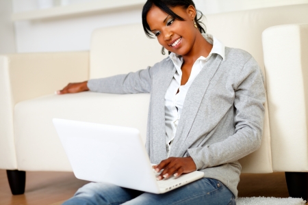 Portrait of a lovely young woman smiling and looking to laptop while is sitting on the floorの写真素材
