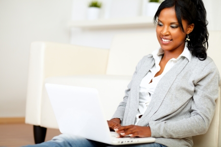 Portrait of a lovely student girl smiling and looking to laptop screen at home indoorの写真素材
