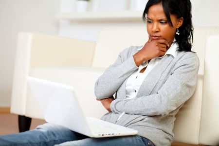 Portrait of a pensive attractive young woman sits on the floor in front of her laptop at home indoorの写真素材
