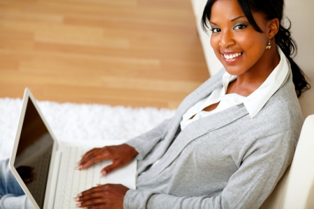 Top view portrait of a young woman with her laptop smiling at you while sitting on the floor at home indoorの写真素材