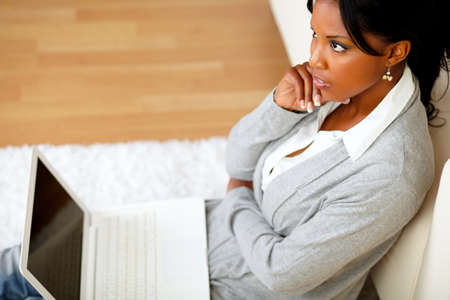 Top view portrait of a pensive young woman is sitting on the floor in front of her laptop at home indoorの写真素材