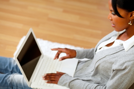 Portrait of a charming young woman pointing to laptop screen while sitting on floor at home indoorの写真素材