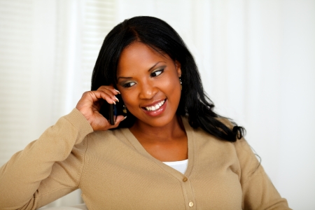 Portrait of an afro-American woman conversing on mobile phone at home indoorの写真素材