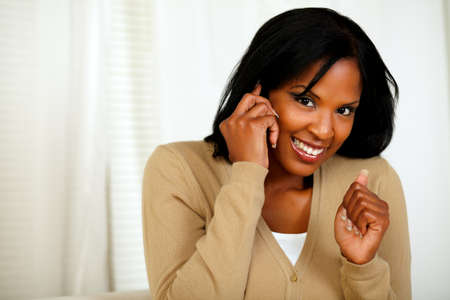 Portrait of an excited woman looking to you and conversing on mobile phone at home indoorの写真素材