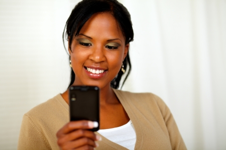 Portrait of a charming black woman sending a message by cellphone at soft colors compositionの写真素材