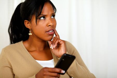 Portrait of a pensive black woman using her cellphone at soft colors compositionの写真素材