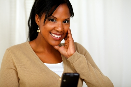 Portrait of a smiling woman looking at you sending a message with her cellphone at soft colors compositionの写真素材