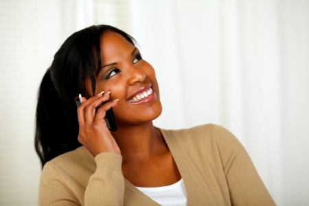 Portrait of a pretty woman looking up while talking on cellphone at home indoorの写真素材