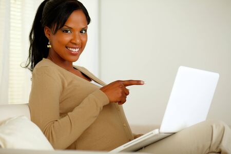 Portrait of a young woman pointing the laptop screen while smiling at youの写真素材