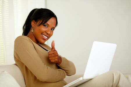 Portrait of a positive young afro-American woman in front her laptop while looking at you and lifting the finger upの写真素材