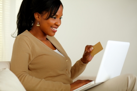 Portrait of a young woman in front her laptop while holding a gold credit card and browsing the Internet at home indoorの写真素材