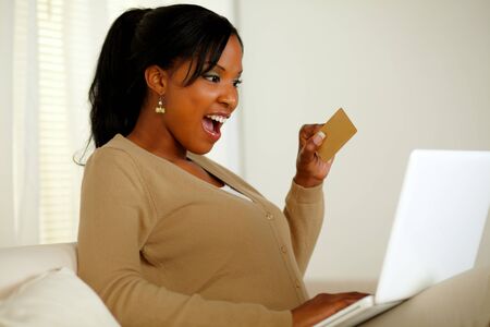Portrait of a charming young woman holding a gold credit card while buying on the Internet with her laptop at home indoorの写真素材