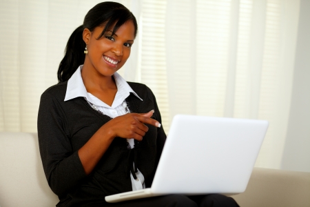 Portrait of a woman on black suit pointing to laptop screen while sitting on sofa at home indoor and looking at youの写真素材