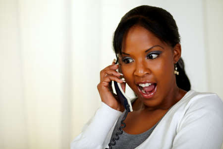Portrait of an excited young woman screaming and talking on phone at soft colors compositionの写真素材