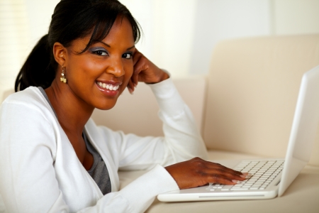Portrait of a young woman looking at you while browsing the Internet at home indoorの写真素材
