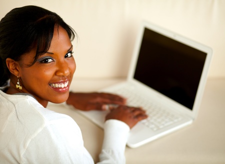 Portrait of a stylish female looking at you while working on laptop at home indoor. With copyspaceの写真素材