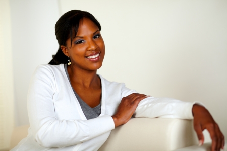 Portrait of a lovely young woman smiling and looking at you while sitting on couch. With Copyspaceの写真素材