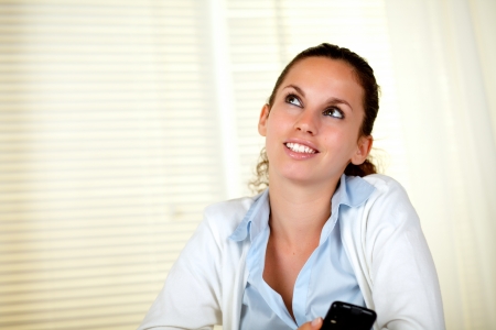 Pensive young woman looking up with cellphone at home - copyspaceの写真素材