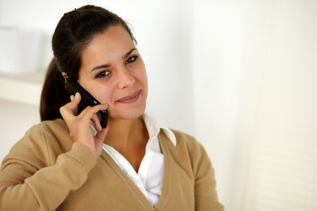 Portrait of a charming young woman conversing on mobile phone while is looking at youの写真素材
