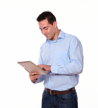 Portrait of a charismatic young man on blue shirt looking at his tablet pc while standing on isolated backgroundの写真素材