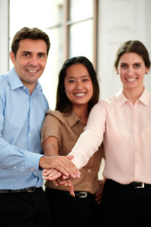 Portrait of group of business people with hands together in unity sign smiling at you and standing...