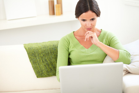 Waist up portrait of a concentrated person using a laptop while sitting inside the houseの写真素材