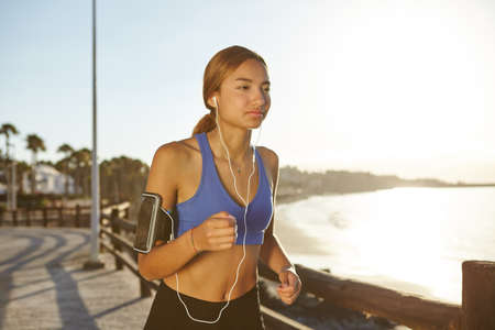 Waist up portrait of a young female running outside at dawn for a healthy livingの写真素材