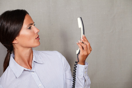 Young businesswoman looking angry at the phone without speaking on grey texture background