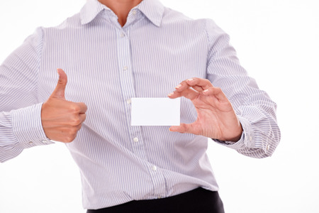 Cropped businesswoman, wearing a button down shirt, gesturing a thumbs up sign with one hand and holding a blank visit card with the other hand on a white backgroundの写真素材