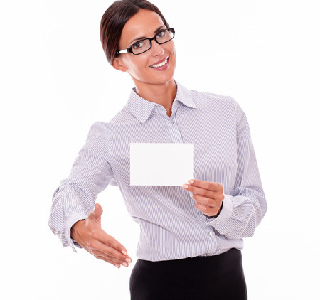 Smiling brunette businesswoman with glasses, wearing her long hair tied back, and a button down shirt, holding a blank copy space in one hand, with the other hand out in a greeting gestureの写真素材