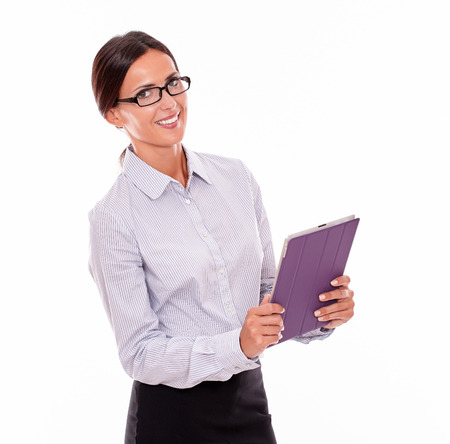 Smiling brunette businesswoman with glasses carrying a tablet, wearing her straight hair tied back and a button down shirt, looking at the camera with the tablet in both hands, on a white backgroundの写真素材