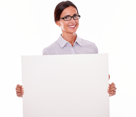 Smiling brunette businesswoman, wearing her hair tied back and a button down shirt, holding a blank placard in front of her on a white backgroundの写真素材
