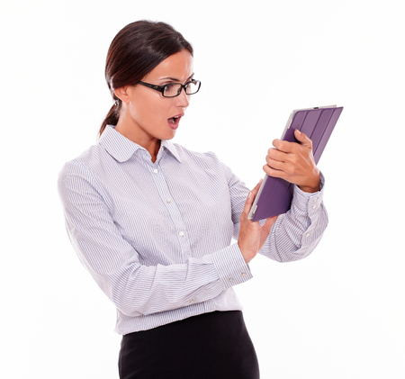 Surprised businesswoman using a tablet while looking at the tablet with her mouth open, wearing her straight hair back and a button down shirt on a white backgroundの写真素材