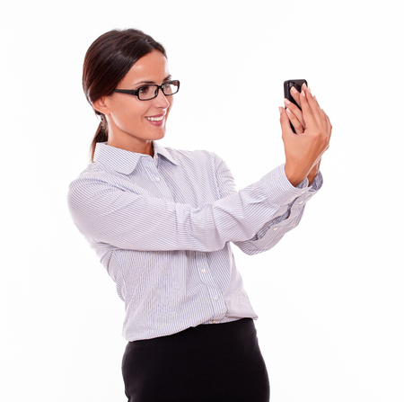 Smiling businesswoman taking selfies with her cell phone with a happy smile while wearing her straight hair back and a button down shirt on a white backgroundの写真素材