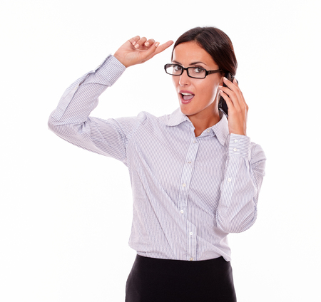 Planning businesswoman speaking on cell phone while looking at camera and making a gesture with one hand while wearing her straight hair back and a button down shirt on a white backgroundの写真素材
