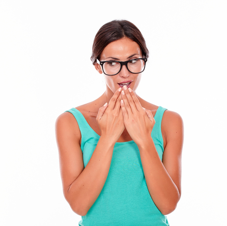 Mistaken caucasian woman with her hands to her mouth while looking at the camera wearing her long hair tied back in a green tank top on a white backgroundの写真素材