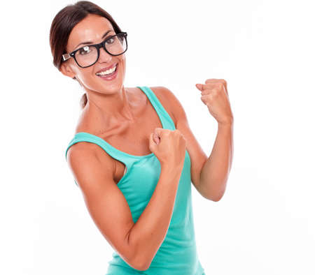 Celebrating adult woman smiling at camera while showing a victory sign with both hands and wearing her long hair tied back in a green tank top on a white backgroundの写真素材