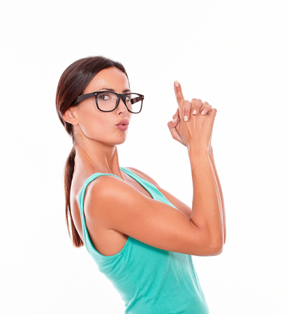 Pouting woman pointing at copy space above her head with both hands while looking at the camera with a charismatic smile and wearing her long hair tied back in a green tank top on a white backgroundの写真素材