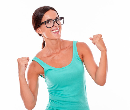 Celebrating adult woman smiling at camera while showing a victory sign with both hands and wearing her long hair tied back in a green tank top on a white backgroundの写真素材