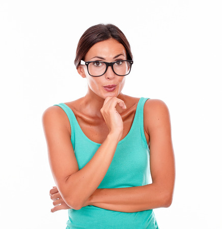 Mistaken caucasian woman with a hand to mouth while looking at the camera as if she made a mistake wearing her long hair tied back in a green tank top on a white backgroundの写真素材