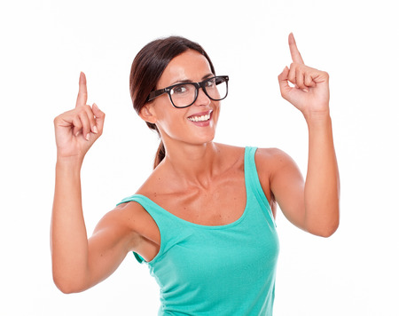 Smiling caucasian adult woman pointing upward with both hands while looking at the camera wearing glasses on a white backgroundの写真素材