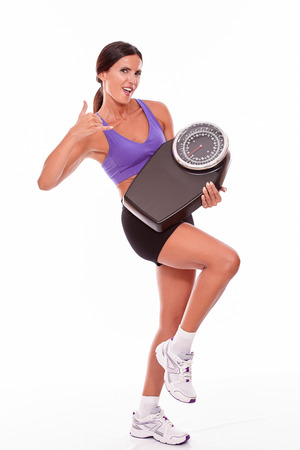 Healthy smiling brunette woman with a scale, gesturing a phone call while looking at the camera with violet and black gymnastic clothing, isolatedの写真素材