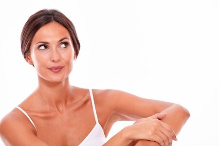 Attractive young woman smiling while looking away dreamily while wearing a white tank top and hair tied back, isolatedの写真素材