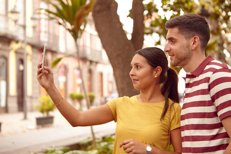 Young couple looking at the cell phone smiling happily while taking a selfie dressed casually in jeans and t-shirtsの写真素材
