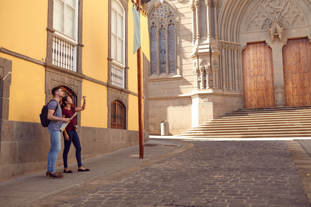 Young tourist couple on vacation with a backpack and map looking up while dressed casually in jeans and t-shirts with an old building behind themの写真素材