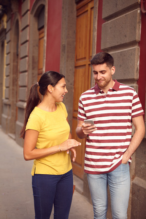 Young couple looking at cell phone while sharing a joke and smiling happily, dressed casually in t-shirts with old buildings behind themの写真素材