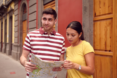 Young couple studying a map and looking right while smiling happily and dressed casually in t-shirts with old buildings behind themの写真素材