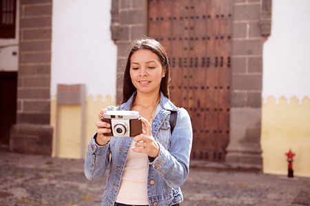Serious young girl taking a picture looking at her camera smiling and her hair loose wearing casual clothing in front of a steel doorの写真素材
